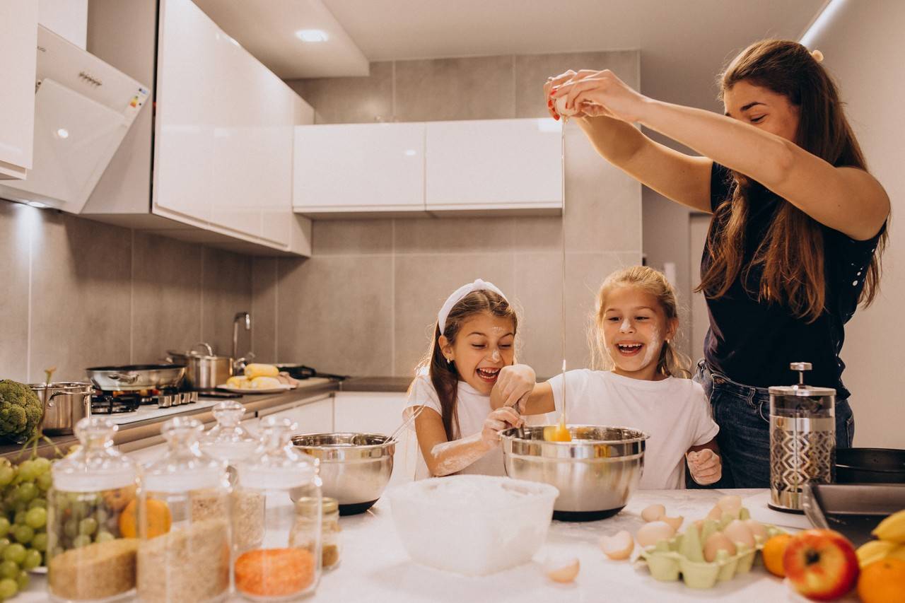 Mãe com duas filhas na cozinha preparando uma receita juntas