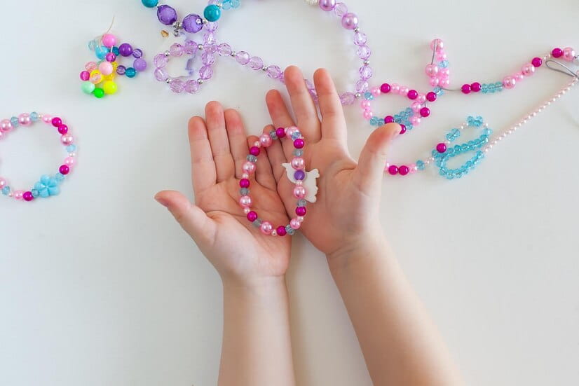 Mãos de criança segurando pulseiras de miçangas coloridas