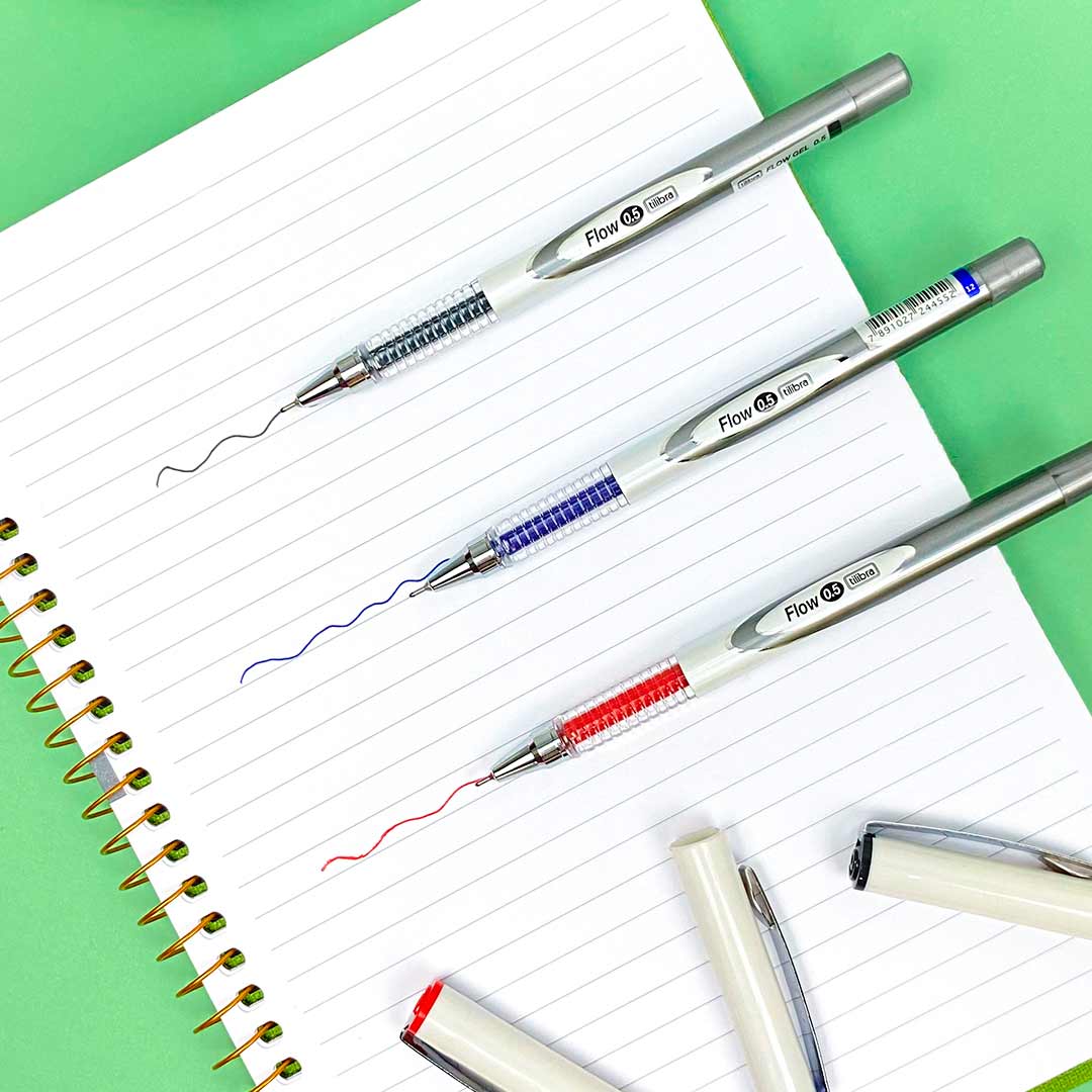 Imagem de caderno espiral com linhas de teste de caneta gel, imagem possui canetas em cima do caderno