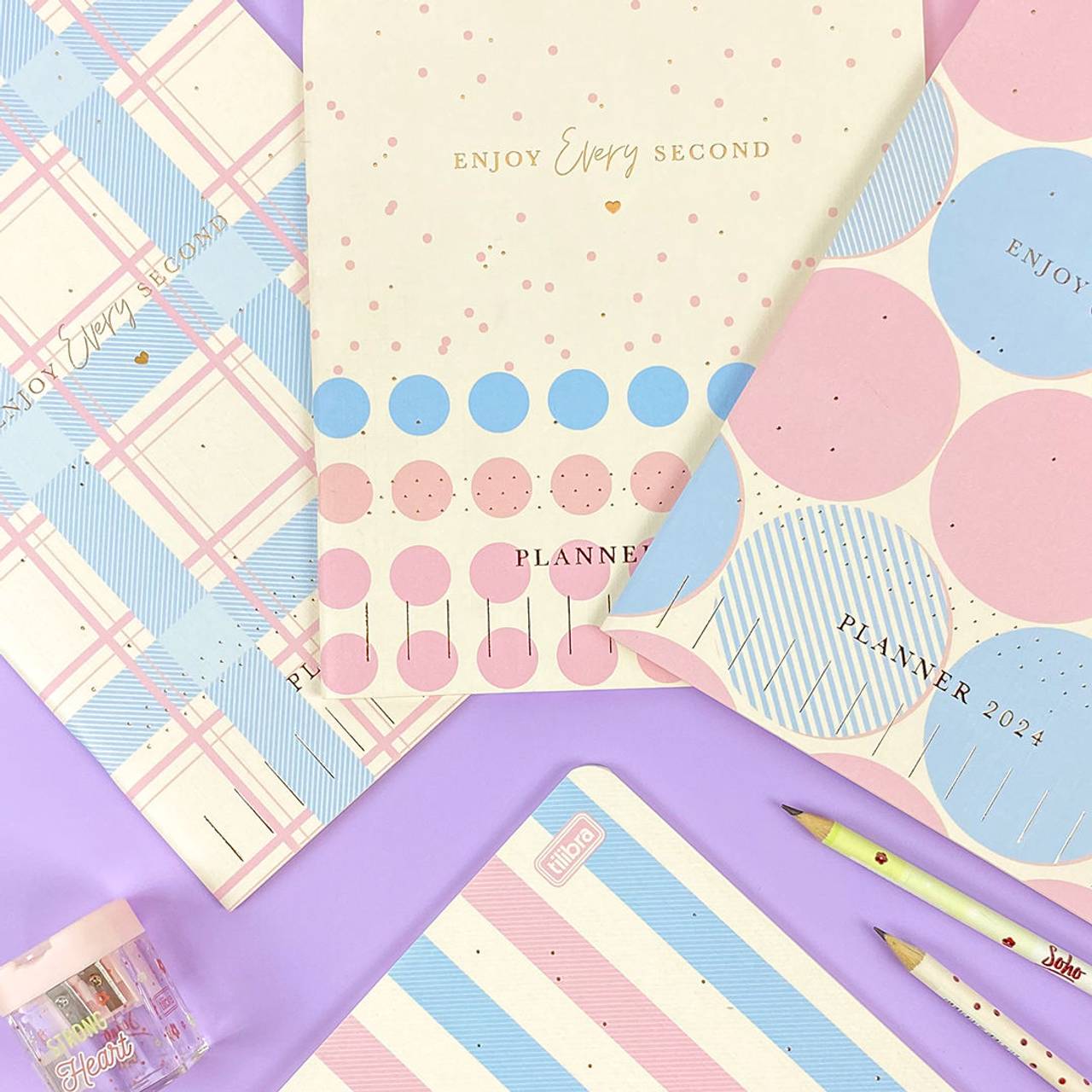 Planners grampeados Tilibra da coleção Soho 2024. Designs em pastel com padrões de bolinhas e linhas, sobre fundo roxo e azul.