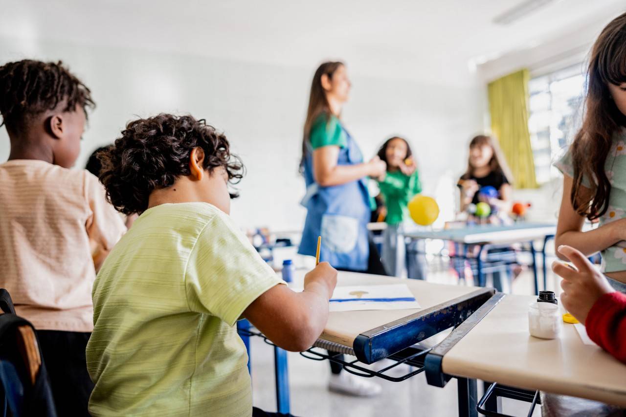 Criança sentada em cadeira escola escrevendo em seu caderno