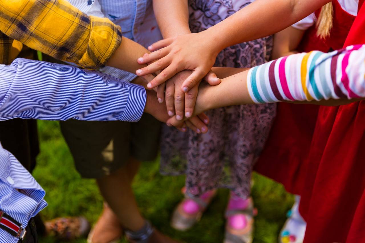 Crianças em cirulo com as mãos no meios, uma sobre as outras