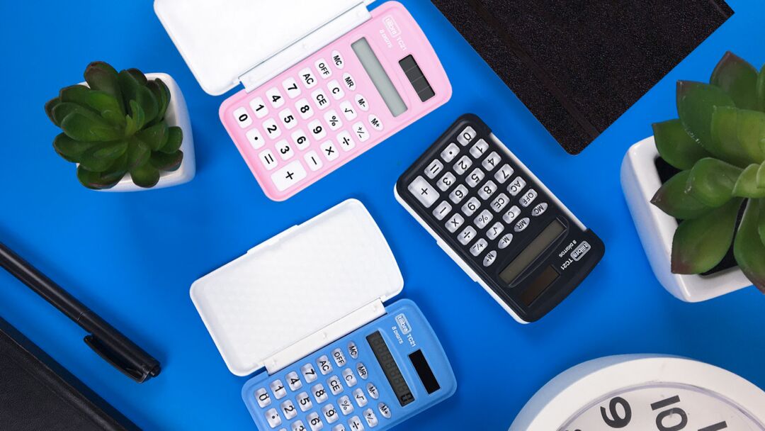 Calculadoras coloridas sobre mesa azul com plantas.