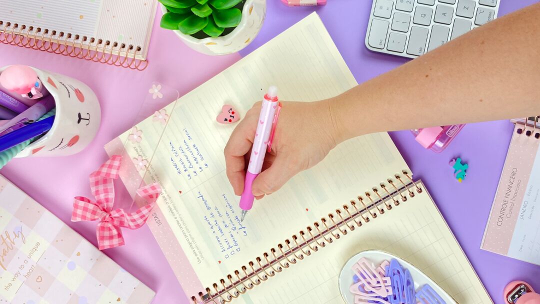 Pessoa escrevendo em caderno colorido com caneta rosa.