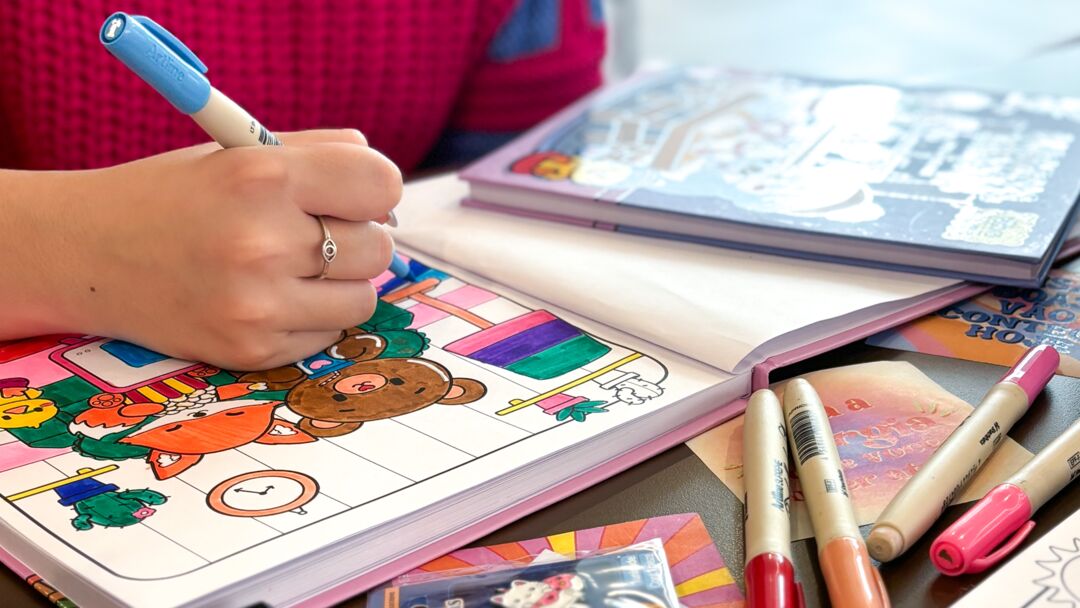 Pessoa colorindo em caderno com canetinhas coloridas
