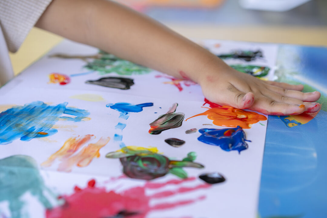 Criança pintando com as mãos em papel colorido.