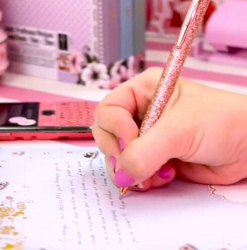 Mão feminina escrevendo com caneta em papel decorado.