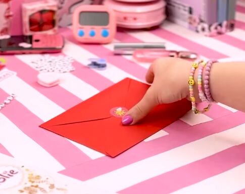 Mão segurando um envelope vermelho sobre uma mesa rosa