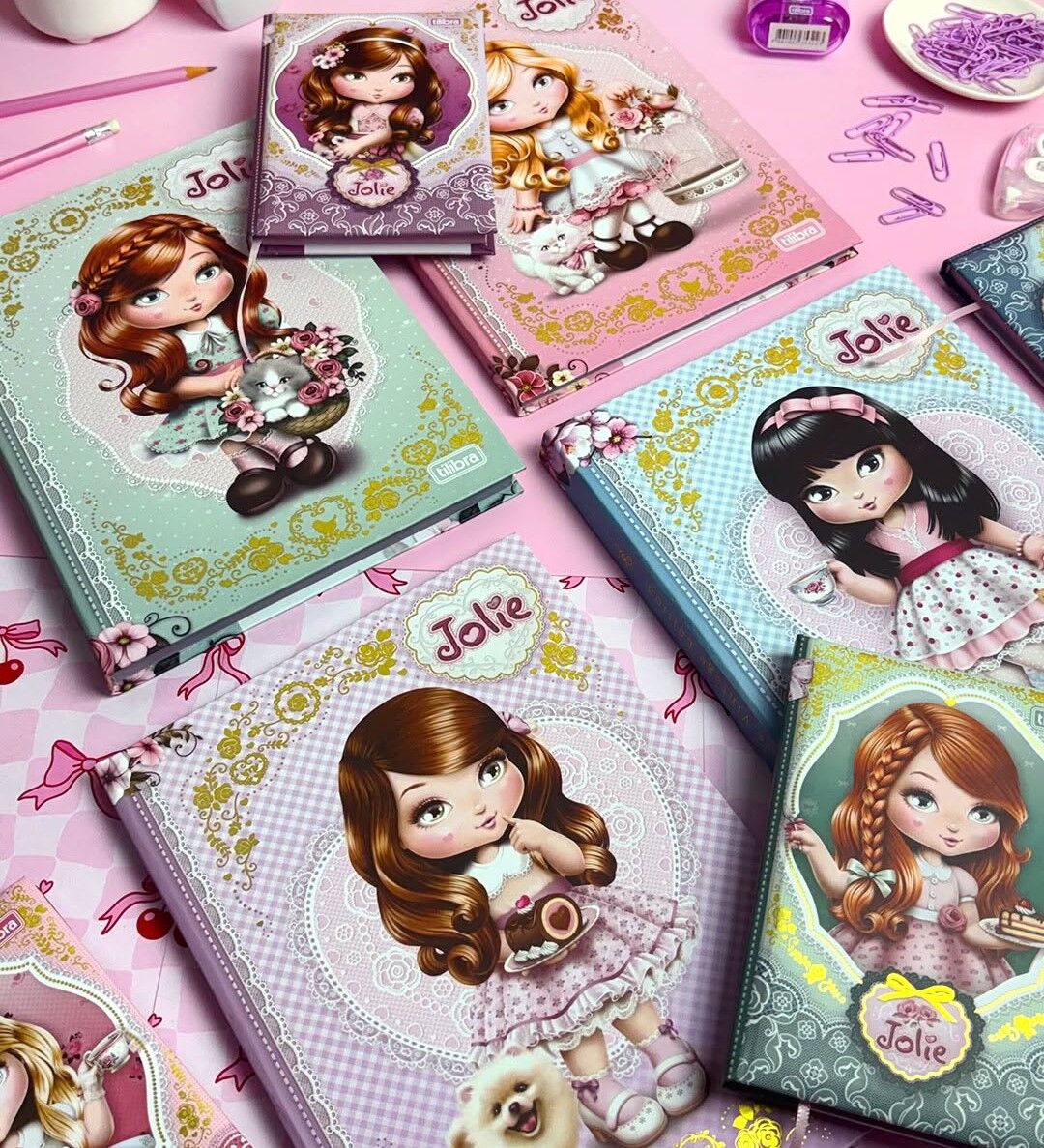 Vários cadernos de personagens Jolie em mesa rosa.