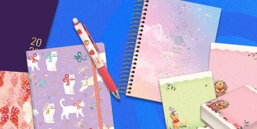 Cadernos e caneta coloridos sobre fundo azul.